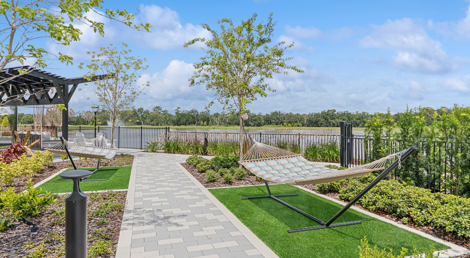 Orlando, FL, Luxury Apartments with In-Unit Washer and Dryer - Ascend Nona West - Hammock Lawn with a Pergola and Two Hammocks on Green Lawn, Surrounded by a Metal Fence and Landscaping.