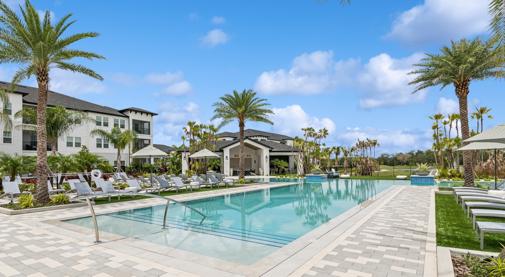 Two-Bedroom Luxury Apartments in Orlando, FL with In-Unit Washer and Dryer - Ascend Nona West - Resort-Style Saltwater Pool Surrounded by Daybeds, Loungers, and Umbrellas, Trees, Overlooking the Apartments.