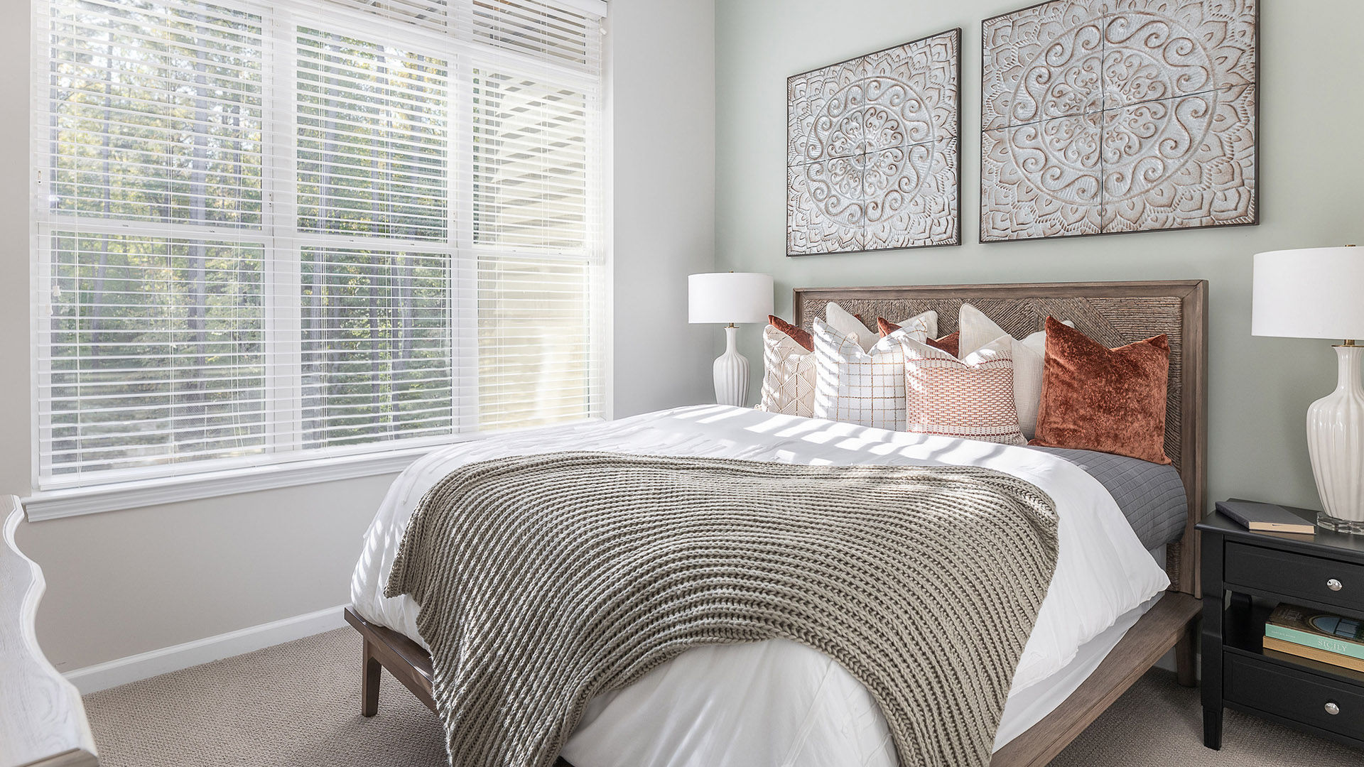 Modern senior apartment bedroom with knitted blankets on a bed and art pieces on the wall above