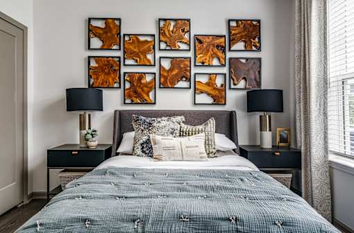 A bed with a blue comforter and pillows is in front of a wall with framed leaves.