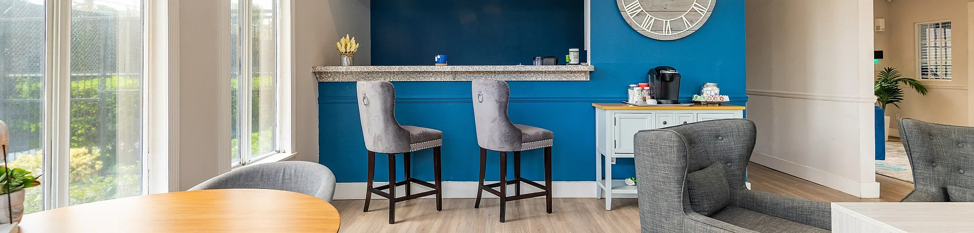 Chic apartment lounge featuring a modern café-style breakfast bar, plush seating, and natural light from large windows.