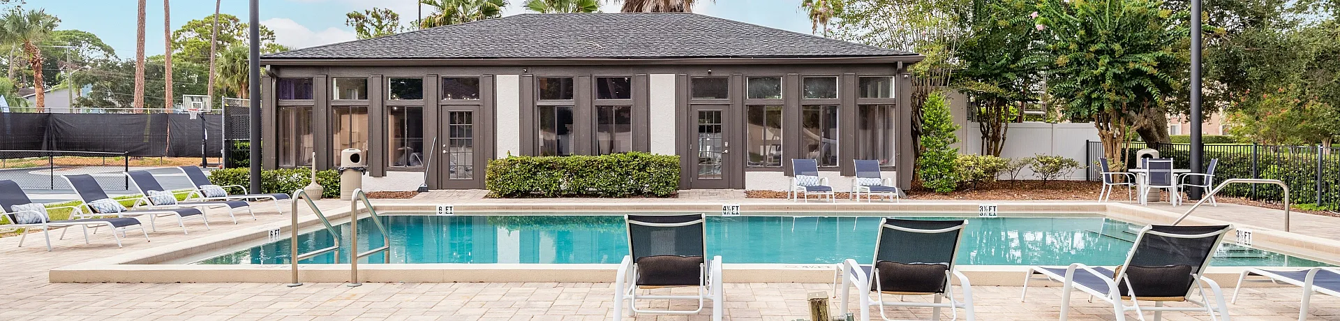 Luxurious apartment community showcasing a pristine swimming pool, elegant lounge chairs, and a stylish clubhouse surrounded by lush greenery.