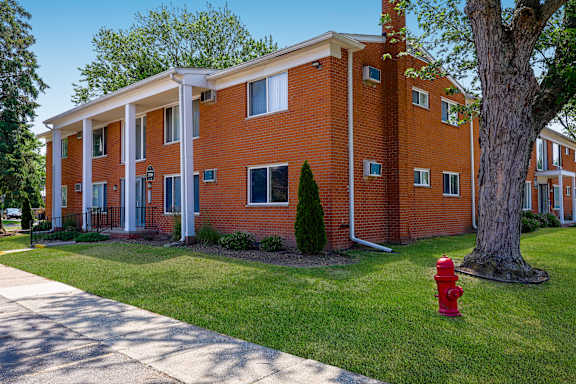 A red fire hydrant sits on a green lawn in front of a red brick building.