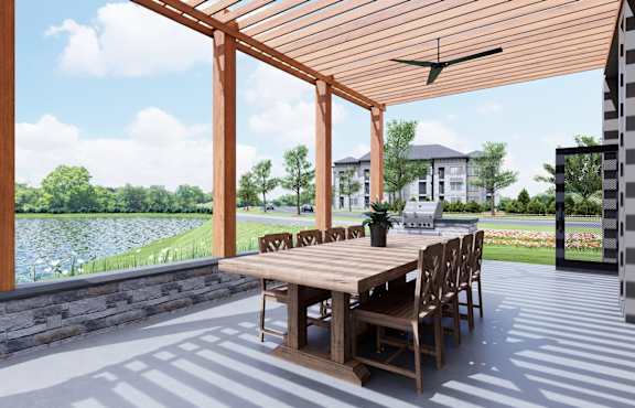 A wooden table and chairs are set up on a patio with a lake and house in the background.