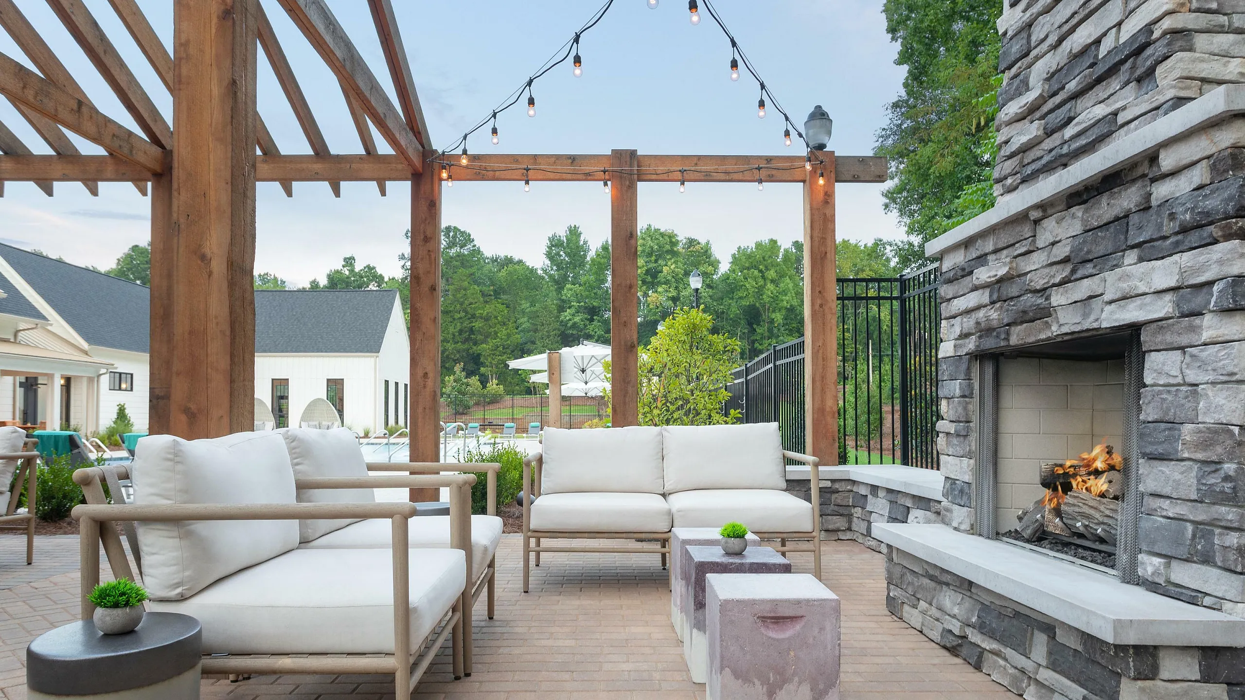 Charming outdoor patio with modern white seating, rustic wooden pergola, and a cozy stone fireplace. Perfect for relaxation and entertaining.