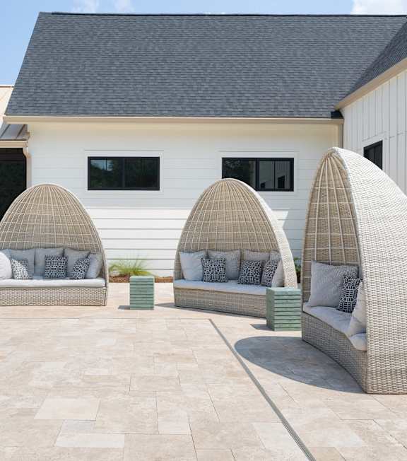 A white house with a pool and three wicker chairs.
