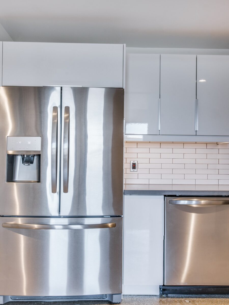 Kitchen with gloss white cabinets, stainless steel appliances, tiled backsplash.