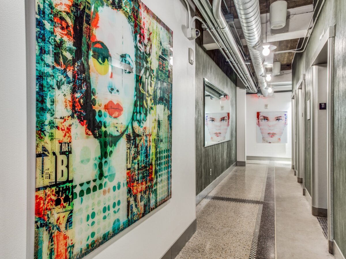 Community hallway near elevators with hard flooring, decorative artwork on walls, decorative wood paneling, exposed industrial air ducts.