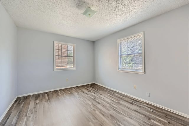 Empty bedroom with light gray walls, wood-look flooring, and two windows with blinds.