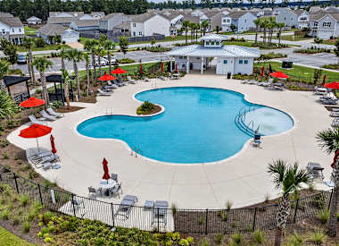 A large swimming pool surrounded by a black fence and red umbrellas.