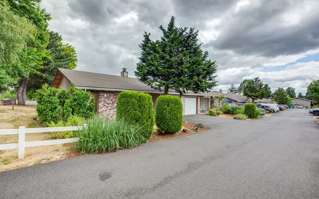 A street view of a residential neighborhood, featuring houses and trees under a cloudy sky.