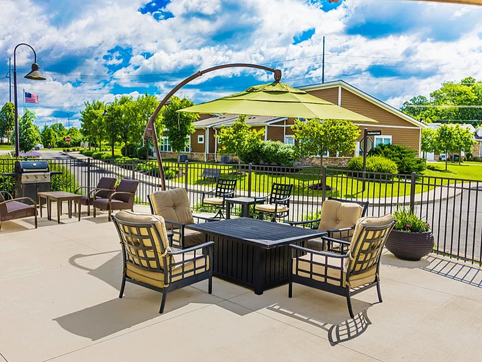 Charming outdoor patio with cozy seating and a modern barbecue grill, set against a backdrop of lush greenery and a bright blue sky.
