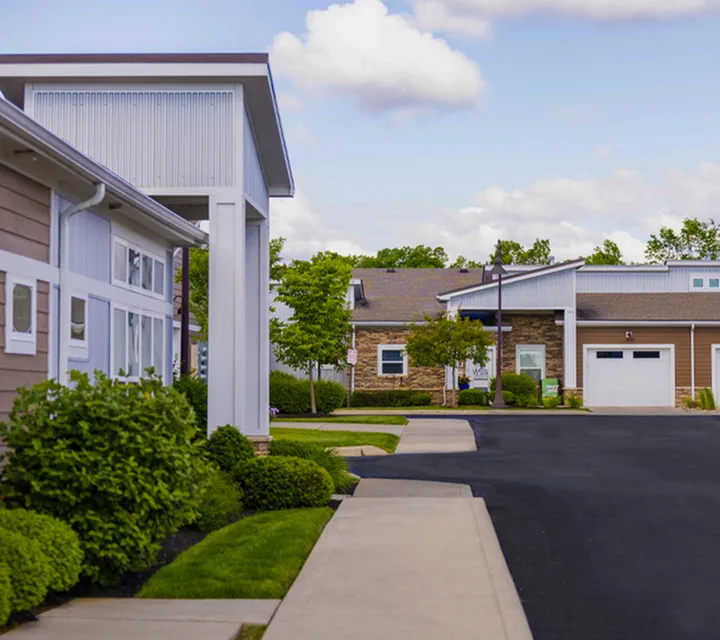 Charming suburban street lined with modern townhouses, lush greenery, and blue skies, perfect for a tranquil lifestyle.