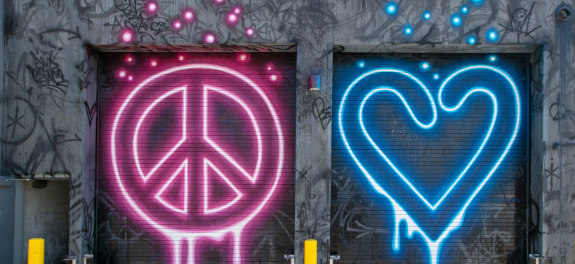 A red neon peace sign and a blue neon heart mural side-by-side on a wall