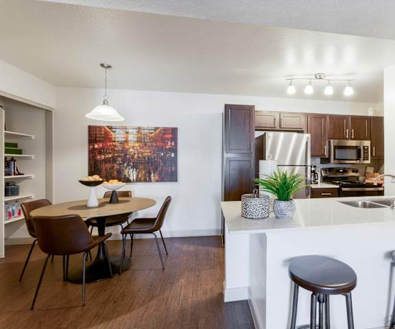 A kitchen with a table and chairs in the foreground and a kitchen in the background.