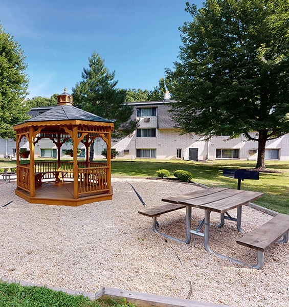 A gazebo sits in a gravel area next to a picnic table.