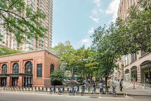 A red brick building with arched windows sits between a tree and a tall building.