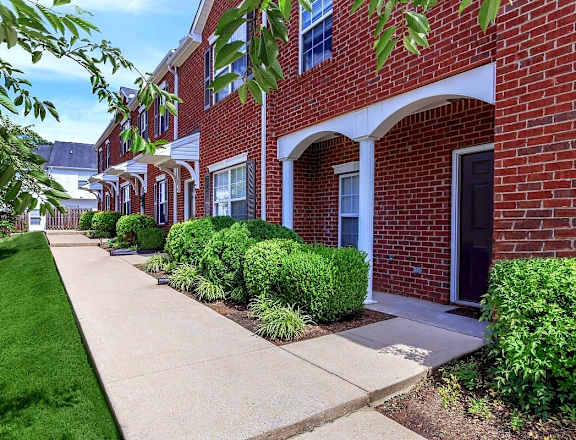 A row of red brick houses with green bushes in front.