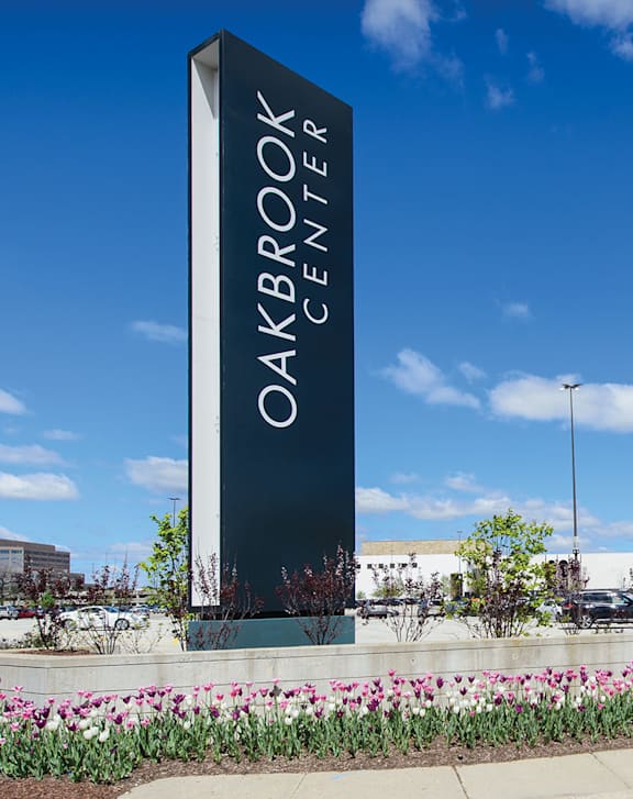 A tall sign that says Oakbrook Center stands in front of a parking lot.
