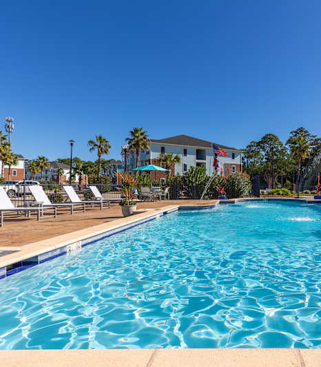 A pool surrounded by chairs and a building in the background.