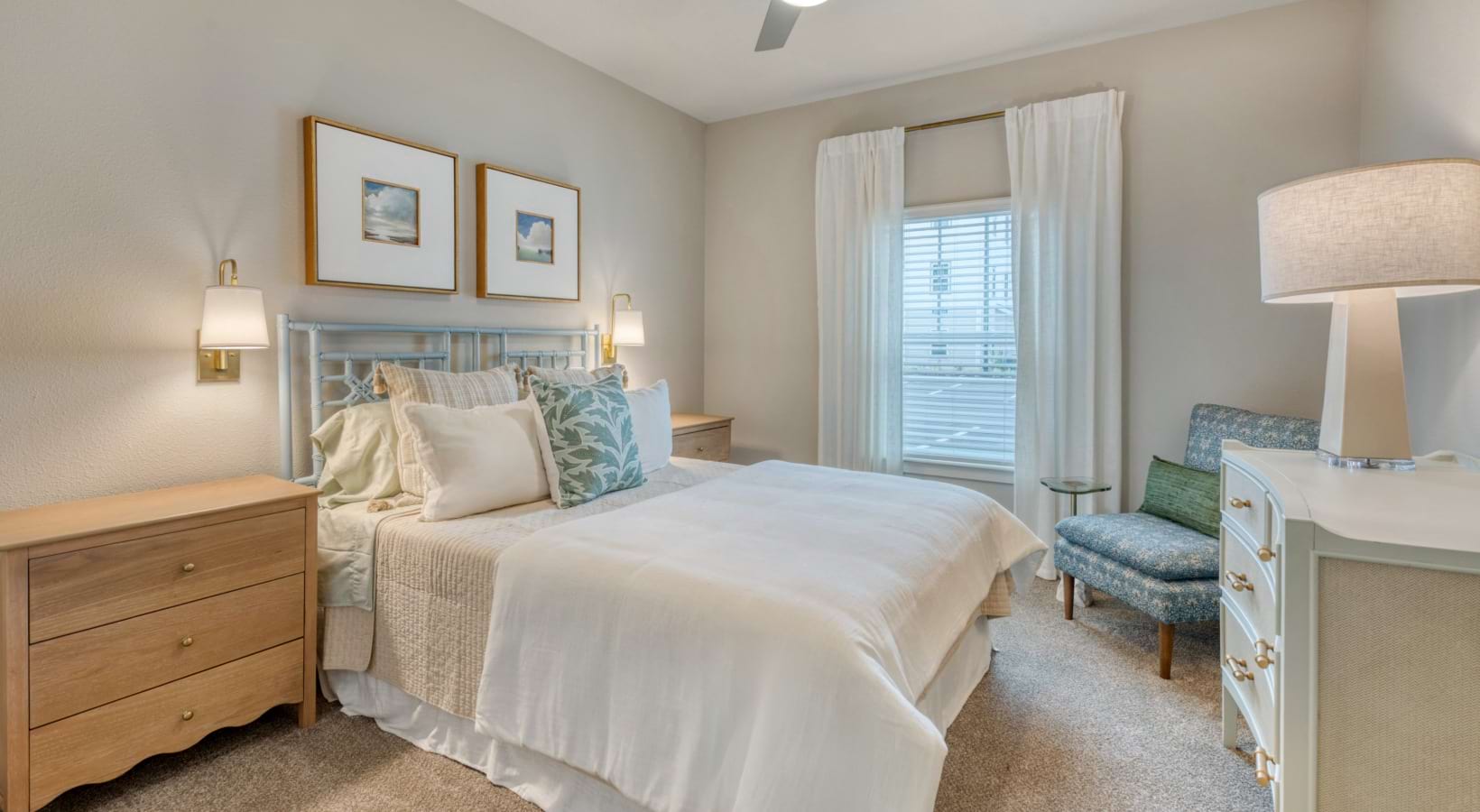 a luxurious bedroom with dresser, bedside tables, accent chair, & wall mounted lights