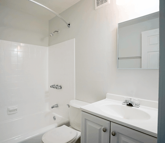A white bathroom with a toilet, sink, and mirror at Dutch Village Apartments, Maryland MD, 21234