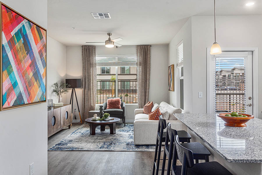 Apartment living area with modern kitchen, comfortable seating, large artwork, and balcony door.