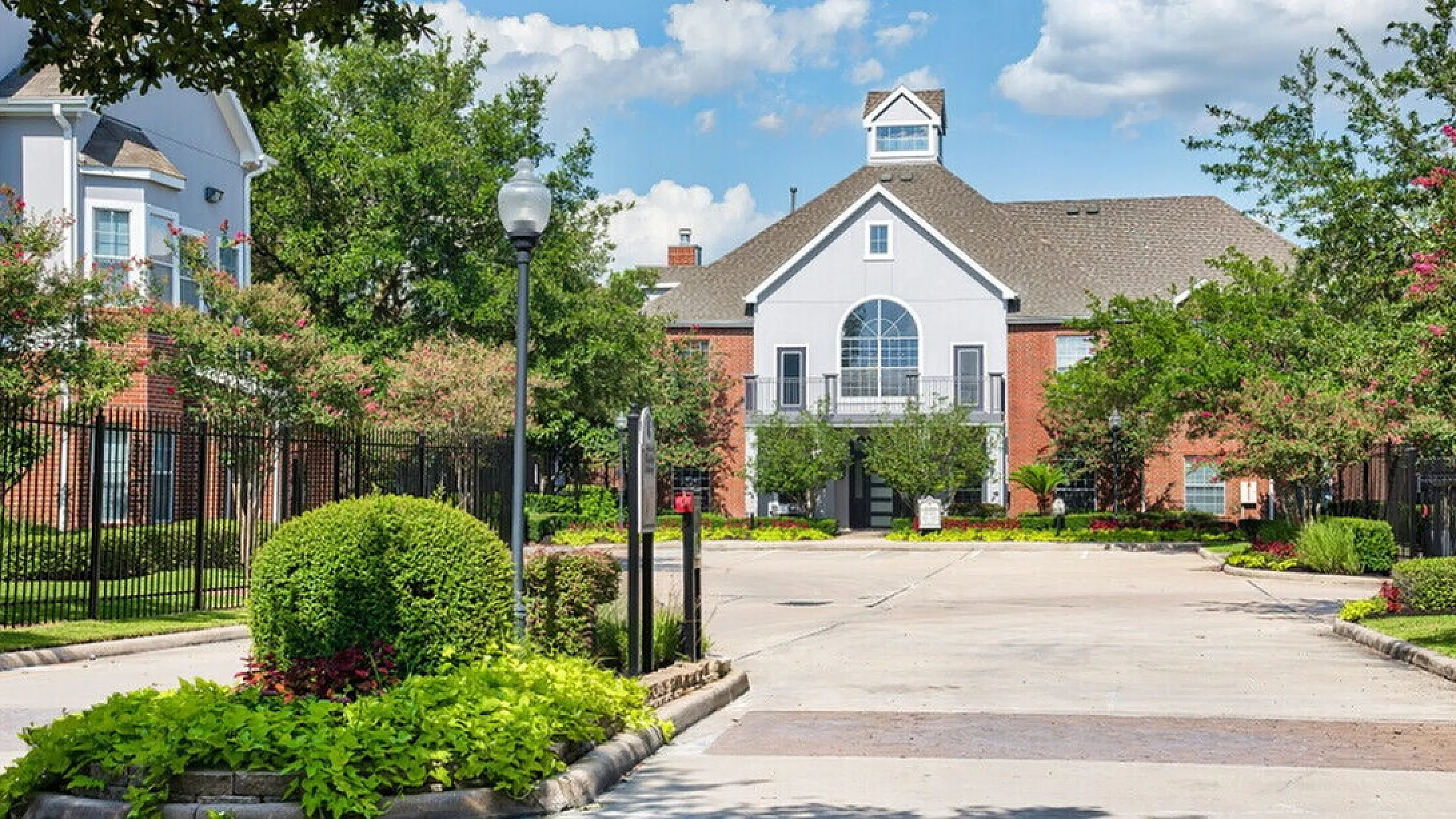 Charming apartment complex with lush greenery and an elegant entrance under a bright blue sky.