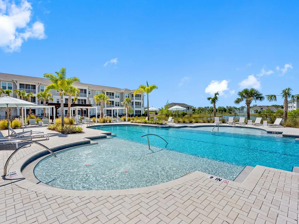 Luxurious apartment complex with a stunning resort-style pool surrounded by lush palm trees and modern amenities, perfect for relaxation and leisure.