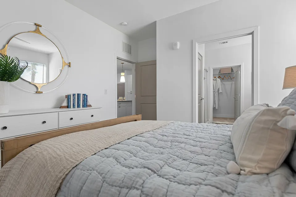 Elegant bedroom with a cozy bed, stylish decor, and a modern dresser with a chic mirror and a lush plant accent.