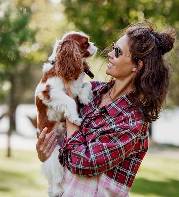 A woman in a plaid shirt is holding a dog in her arms.