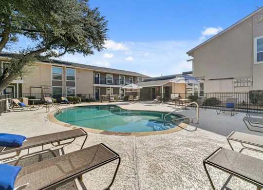 A pool surrounded by chairs and umbrellas in front of apartment buildings.