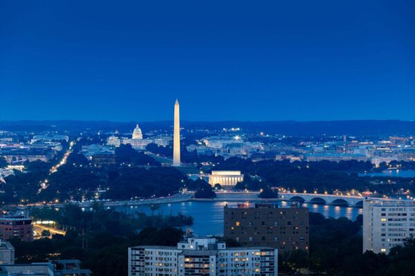 The Washington Monument illuminated at night, reflecting in the calm waters of the Washington River.