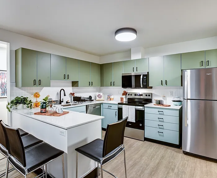 Modern kitchen with stylish green cabinets, sleek stainless steel appliances, and a cozy breakfast bar with seating.