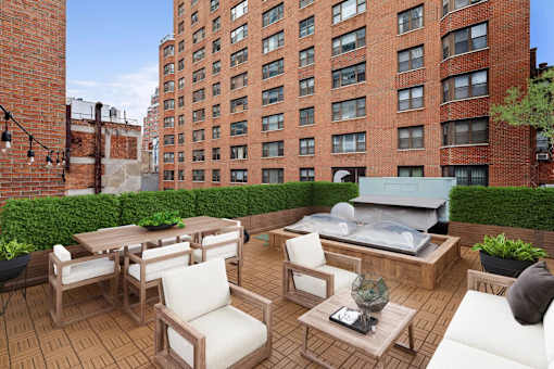 A patio with a table and chairs is surrounded by a brick wall and a green hedge.