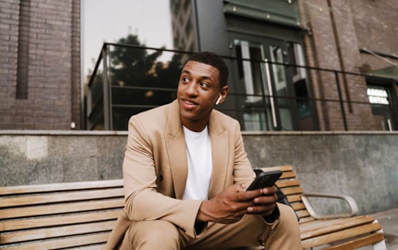 Man in Beige Suit Sitting on a Bench and Holding Phone