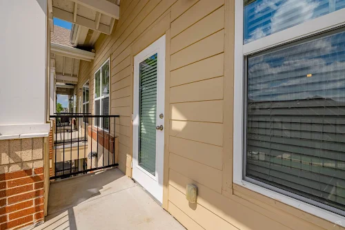 View of a balcony with a door leading into an apartment, featuring wood-style siding and large windows.