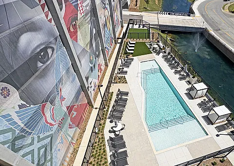 Chic apartment complex with vibrant mural, sleek pool area, and stylish outdoor seating, set against a scenic canal view.