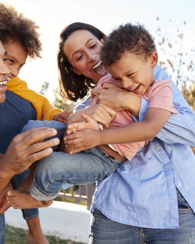 Young mixed race parents playing outdoors carrying their children in the garden