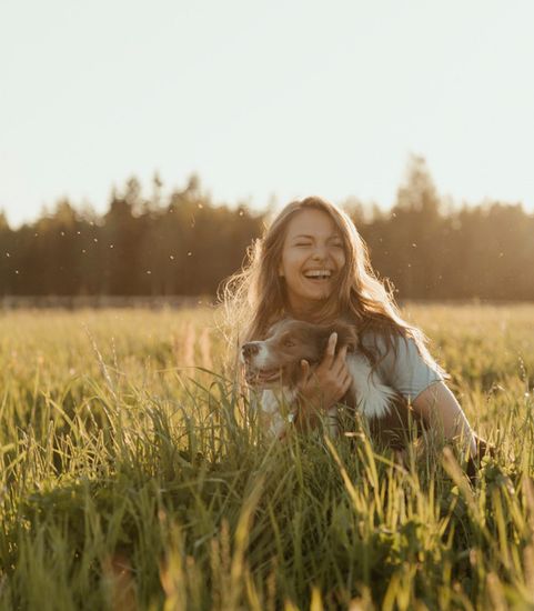 woman hugging dog in grassy field on sunny day