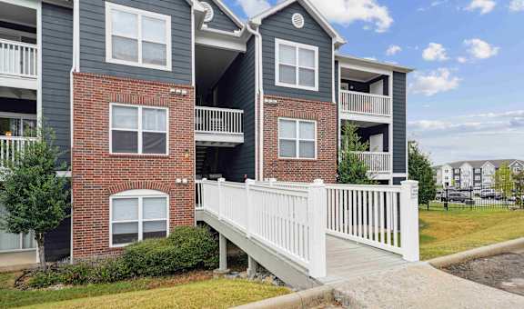 A white fence leads to a brick building with a balcony.