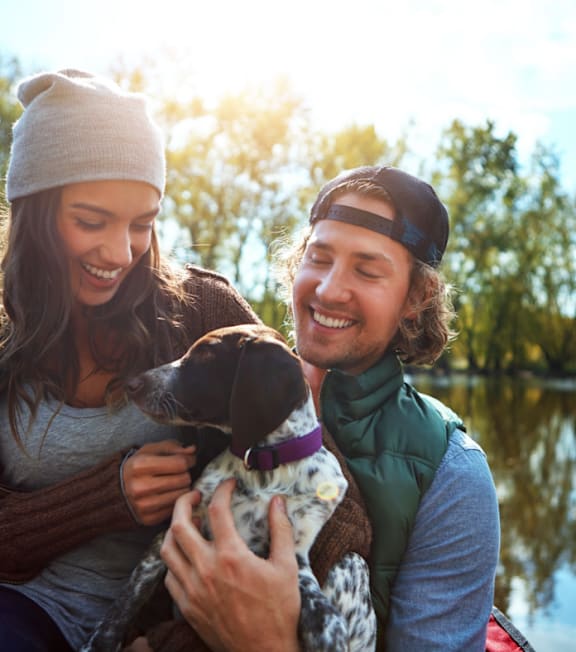 A man and woman are enjoying a sunny day by a lake with their dog.