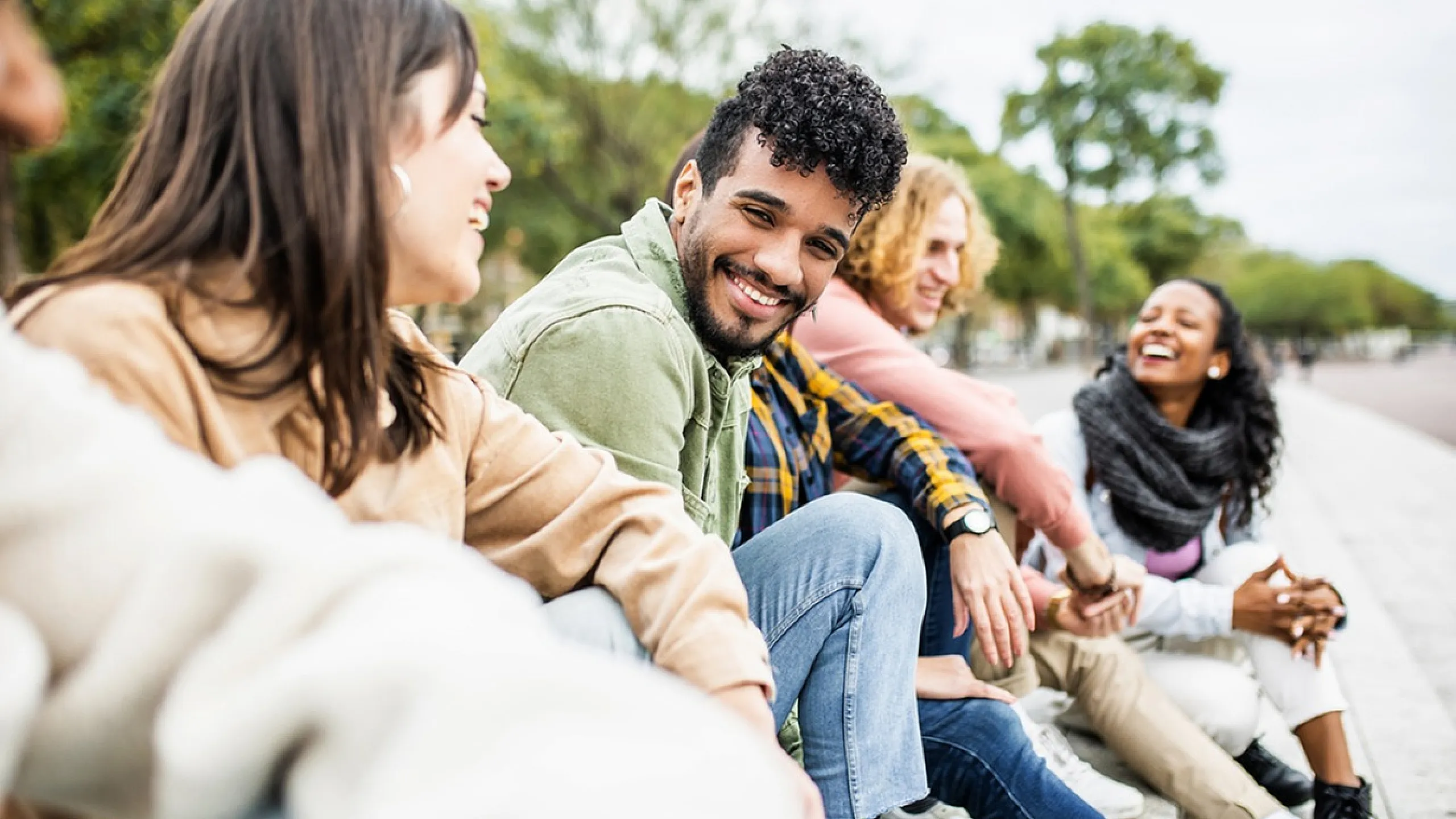 Joyful group of friends sitting outdoors, sharing laughter and positive energy on a sunny day.