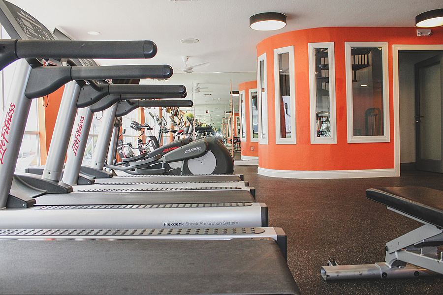 Inviting modern gym with a row of state-of-the-art treadmills and vibrant orange accent wall, perfect for energizing workouts.