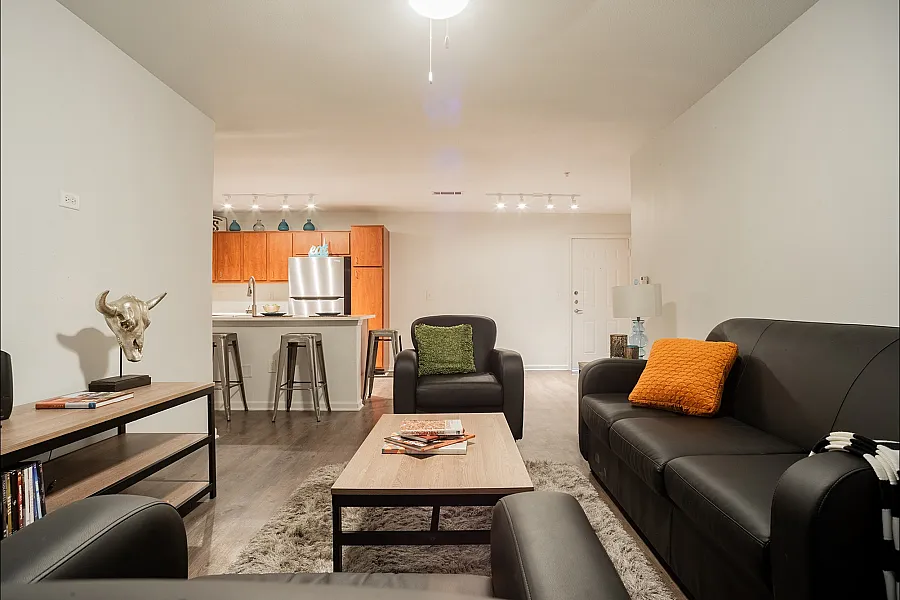 Inviting living room with sleek black leather sofas, vibrant cushions, and a cozy atmosphere, seamlessly flowing into a modern kitchen with stainless steel appliances and stylish bar seating.