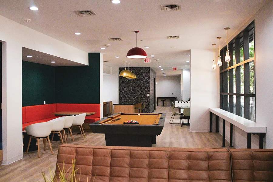 Modern communal space with stylish seating, vibrant lighting, pool table, and spacious dining area, perfect for socializing or working.