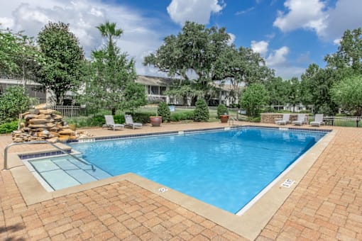 A swimming pool surrounded by a brick patio and trees.
