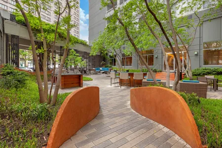 Inviting urban courtyard with lush greenery, modern seating, and barbecue area for outdoor relaxation and social gatherings.