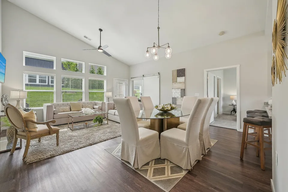 Elegant open-plan living and dining area with sleek hardwood floors, a modern glass-top table, cozy beige sofas, and abundant natural light from large windows.