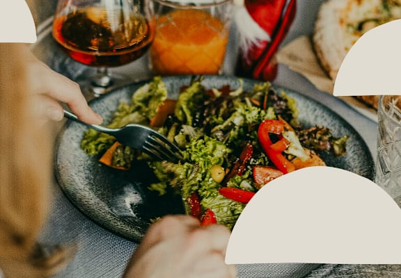 A person is eating a salad at a table with various food items and drinks.